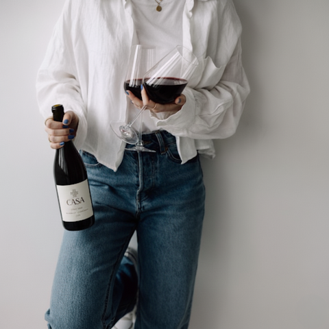 Person holding a bottle and a glass of Casa wine against a plain background